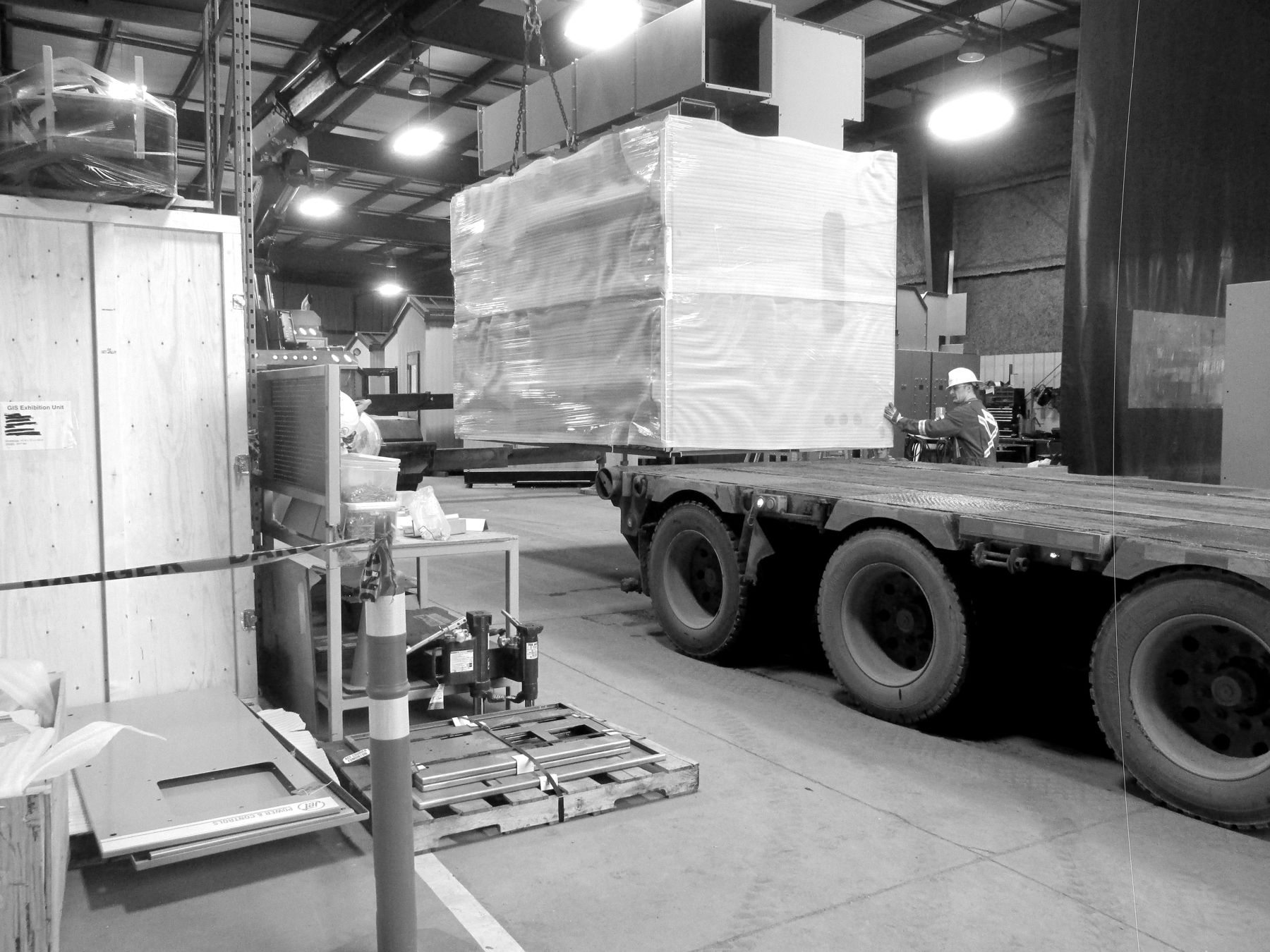 Shop crew loading a wrapped switchgear section onto a trailer inside the plant