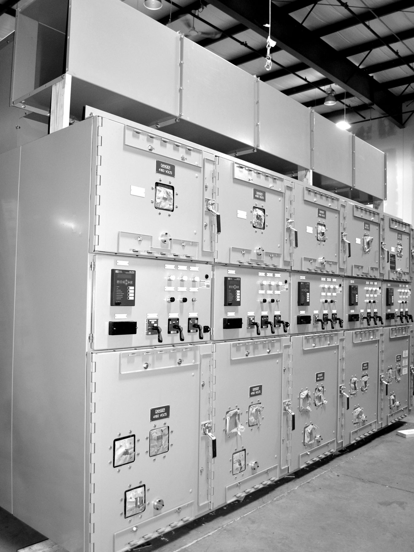 Tall metal-clad switchgear lineup with roof-mounted bus duct on the shop floor