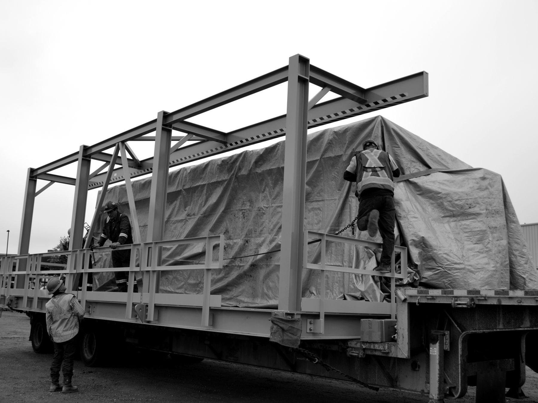 Crew securing a tarped outdoor walk-in switchgear enclosure on a trailer